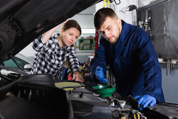 Naklejka na ściany i meble Two workers are replacing the oil in the car on their workplace in workshop.