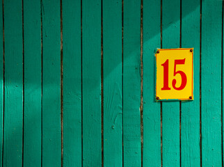 Green flaky paint on an old weathered wooden wall with plate number fiveteen. Wood wall with shadows. Peeling paint flakes.
