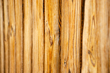 A section of light brown, vertical, overlapped wooden garden fence in closeup. Selective focus side view. Wood background