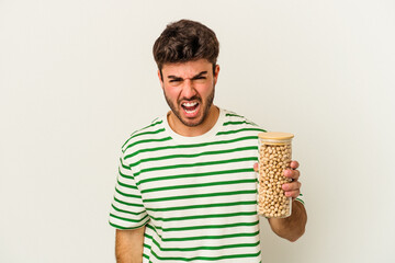 Young caucasian man holding chickpeas jar isolated on white background screaming very angry and...