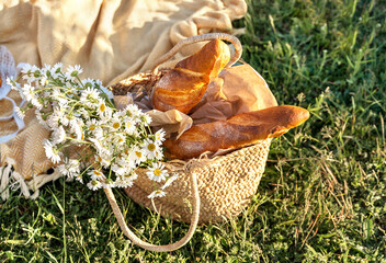 Picnic basket with french baguette decorated with camomile bouquet. Picnic on green grass and...