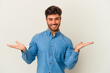Young caucasian man isolated on white background makes scale with arms, feels happy and confident.