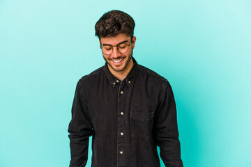 Young caucasian man isolated on blue background laughs and closes eyes, feels relaxed and happy.