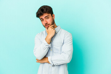 Young caucasian man isolated on blue background suspicious, uncertain, examining you.