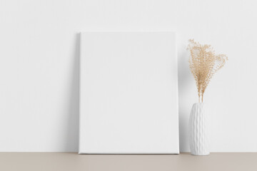 White canvas mockup with a dried flower on the beige table.