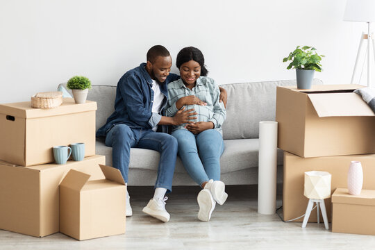 Joyful Pregnant African American Couple Sitting On Sofa In Their New Flat