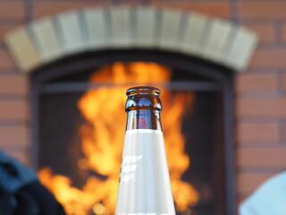 Glass bottle of beer on the background of fire in a home fireplace. The concept of resting by the...
