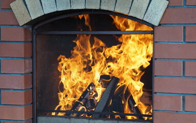 Fire in a stone fireplace in the gazebo of a country house, set up for barbecue, with a protective screen made of metal mesh. Rural life.