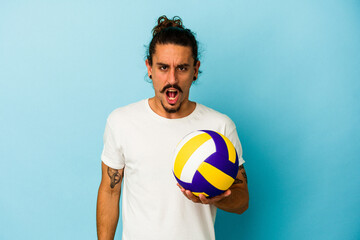Young caucasian man with long hair isolated on blue background screaming very angry and aggressive.