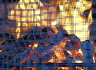 Fire in a stone fireplace in the gazebo of a country house, set up for barbecue, with a protective...