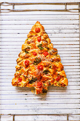 Christmas cake homemade in the form of a Christmas tree with tomatoes and cheese is on the table of white boards. Near Christmas decorations.