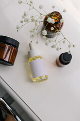 Beauty products female collage on a window sill in a white modern bathroom with blank brand label oil bottle. Minimal flat lay, top view.