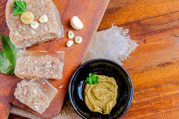  Home jelly, cut into portions lying on the kitchen Board.Near mustard, garlic, Bay leaf, parsley. Place for text.Top view.