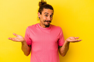 Young caucasian man with long hair isolated on yellow background doubting and shrugging shoulders...