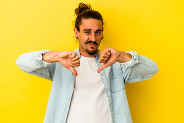 Young caucasian man with long hair isolated on yellow background showing thumb down, disappointment concept.