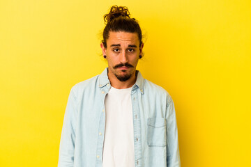 Young caucasian man with long hair isolated on yellow background sad, serious face, feeling miserable and displeased.