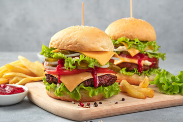 Two homemade hamburgers with meat patty, vegetables and cheese on a gray background. Side view, copy space.
