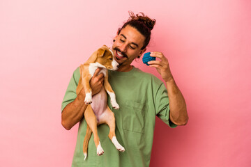 Young caucasian man holding his puppy isolated on pink background
