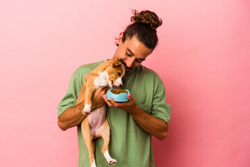 Young caucasian man holding his puppy and his food isolated on pink background