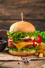 Burger with beef patty, vegetables and cheese and French fries on a brown background. Vertical view, close-up.