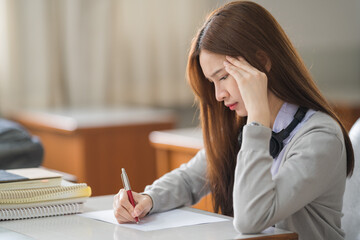 Young desperate and stressful Asian woman student in student uniform doing examination assignment in a college university classroom alone