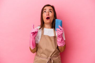 Middle age caucasian woman cleaning home isolated on pink background pointing upside with opened mouth.