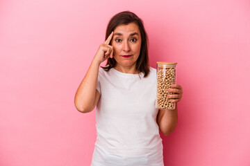 Middle age caucasian man holding a chickpeas jar isolated on pink background pointing temple with...