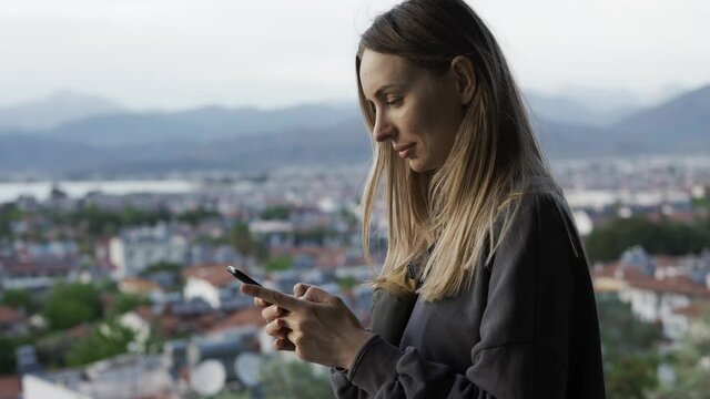 Woman using a smartphone while standing on top view point of the city