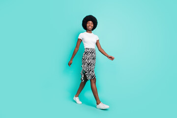 Full body photo of happy afro american pretty lady walk empty space smile isolated on teal color...