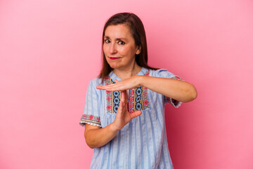 Middle age caucasian woman isolated on pink background showing a timeout gesture.