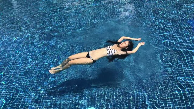 Girl in bikini swimming in an outdoor pool on a sunny day