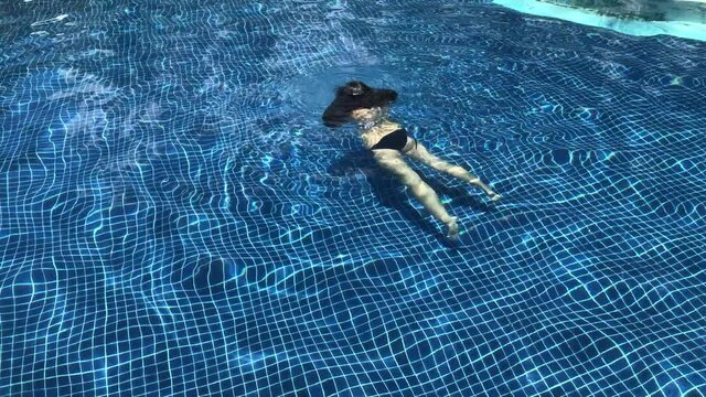 Girl in bikini swimming in an outdoor pool on a sunny day