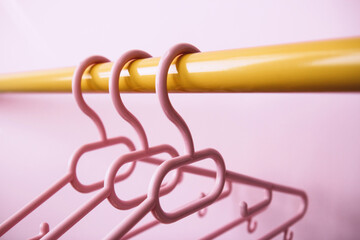 Set of three pink clothes hangers hang on a yellow rack on a pink background