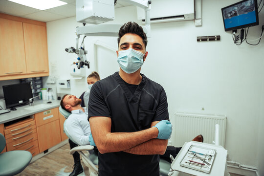 Caucasian male dentist wearing surgical mask and gloves standing by female dentist ready to operate 
