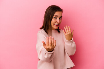 Middle age caucasian woman isolated on pink background pointing with finger at you as if inviting come closer.