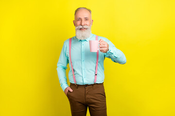 Photo of optimistic old man hold cup wear blue shirt pants isolated on vibrant yellow color...