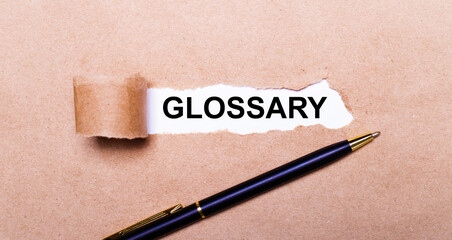 Torn kraft paper, white background with the text GLOSSARY. Nearby is a black handle. View from above - obrazy, fototapety, plakaty