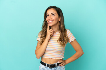 Young woman over isolated blue background thinking an idea while looking up