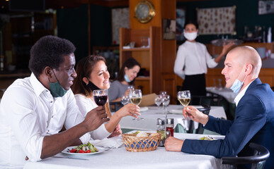 group of frieds in masks sitting and eating in restaurante. High quality photo
