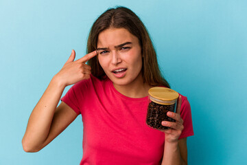 Young caucasian woman holding a coffee jar isolated on blue background showing a disappointment...