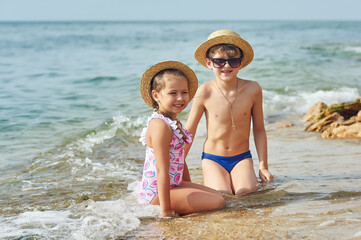 Happy children relax on the sea coast . Brother and sister take a sun bath at the resort .