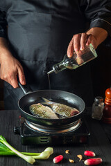 The chef prepares fresh fish in a pan with oil. Preparation for cooking fish food. Working environment in the kitchen of a restaurant or cafe