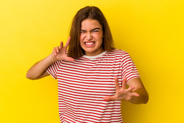 Young caucasian woman isolated on yellow background showing claws imitating a cat, aggressive gesture.