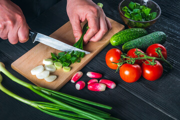 Chef hands close-up cuts young green onions. Cooking salad in the restaurant kitchen. Set of vegetables for a salad diet