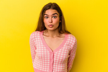 Young caucasian woman isolated on yellow background shrugs shoulders and open eyes confused.