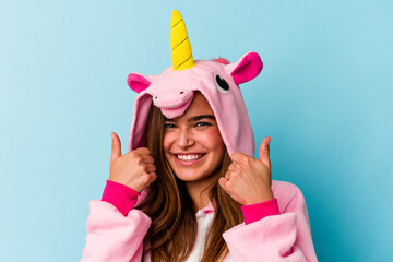 Young caucasian woman wearing an unicorn pajama having fun isolated on blue background