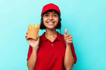 Young mixed race woman fast food restaurant worker holding fries isolated on blue background smiling and raising thumb up