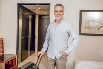 Gray-haired confident man with a suitcase in a hotel room