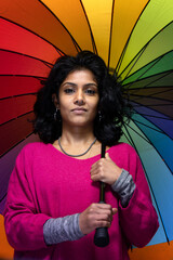 Beautiful Sri Lanka girl poses standing with yellow bright background hanging a colored umbrella - Young woman smiles