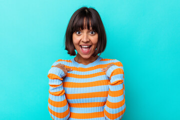 Young mixed race woman isolated on blue background surprised pointing with finger, smiling broadly.